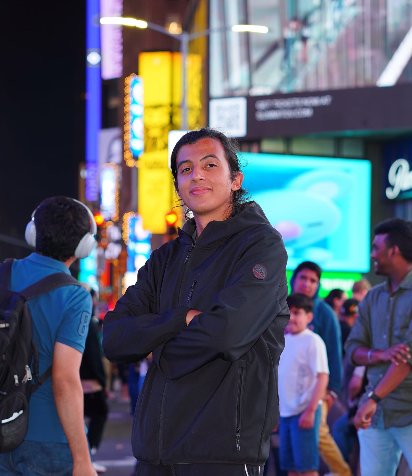 Seif Essam, arms crossed and smiling, on a lit-up city street at night.